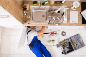 Plumber With Scattered Tools Performing Repair Under Kitchen Sink