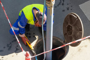 Plumber Peering into Open Manhole During Cleaning of Sewer Line 